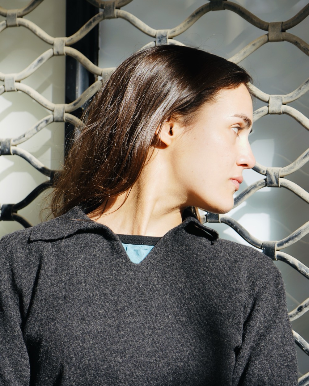 Portrait d'une femme de profil devant une grille métallique