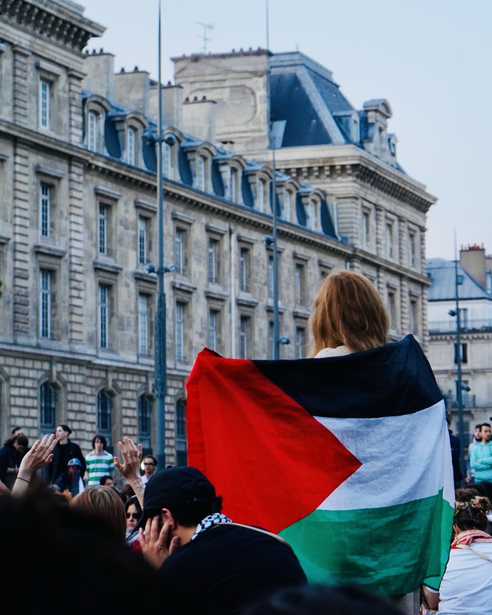 Manifestation à Paris : une personne drapée d'un drapeau palestinien devant un bâtiment
